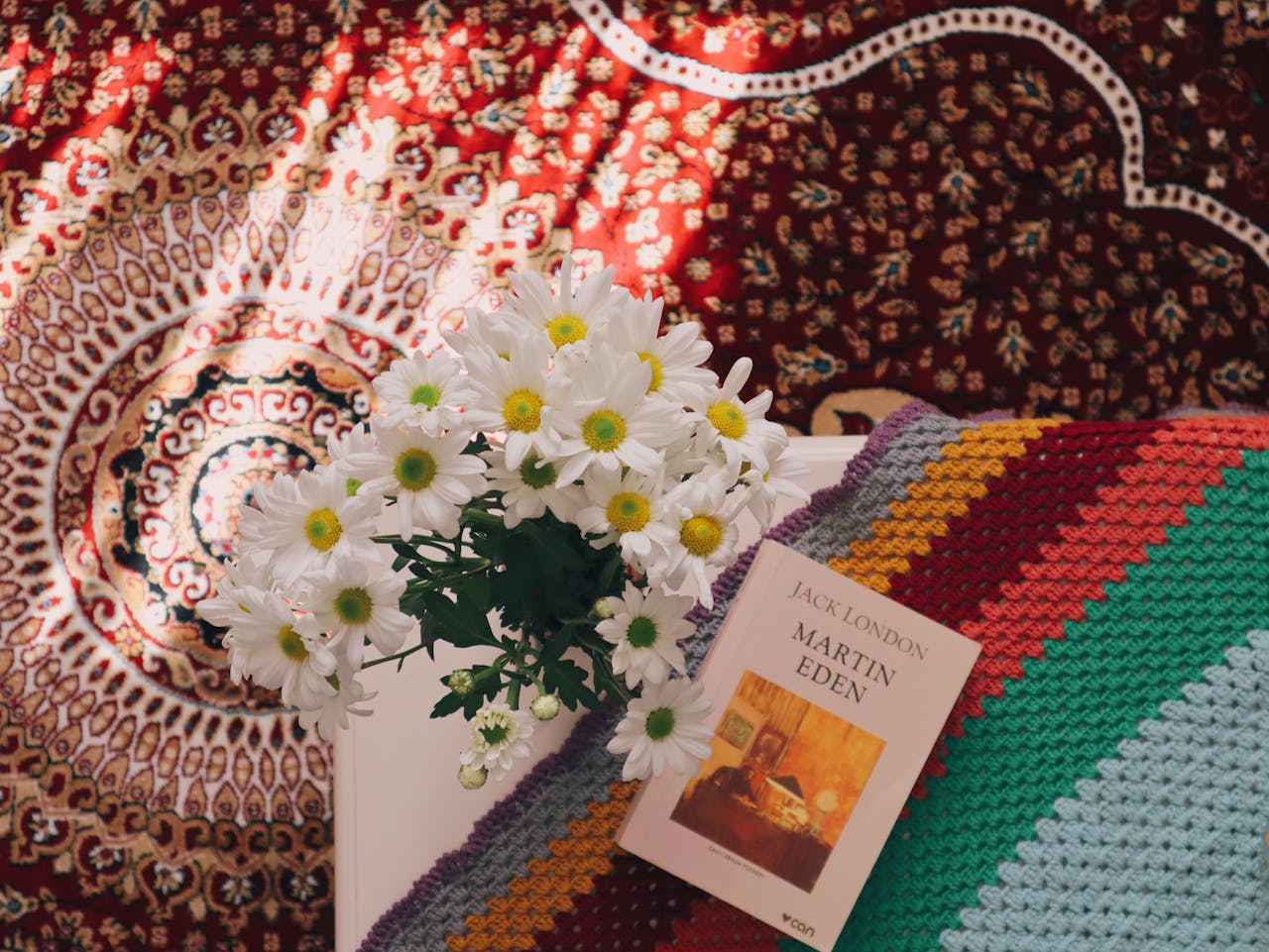 A cozy scene with daisies, a patterned carpet, and the book Martin Eden by Jack London.
