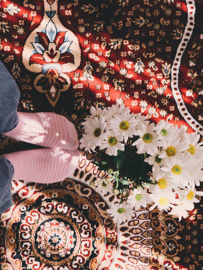 Aerial shot of daisies on a colorful, ornate rug with sunlight casting playful shadows.