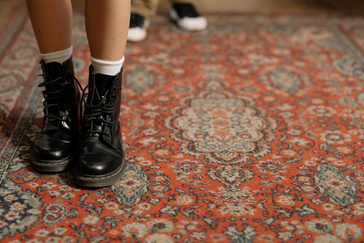 Detail shot of black leather boots on a floral-patterned Persian carpet indoors.