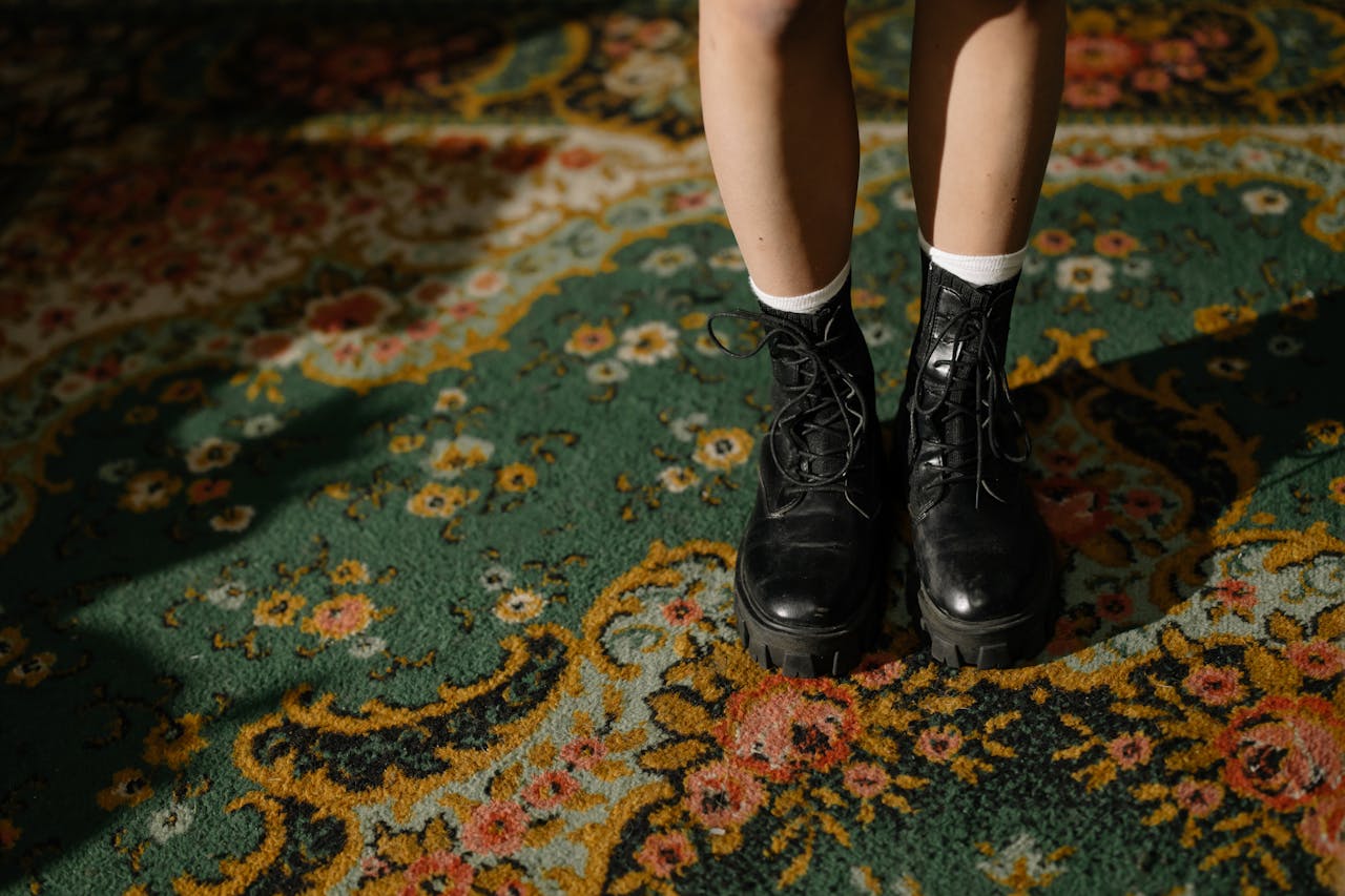 Fashionable black boots on an intricately patterned carpet in a cozy indoor setting.